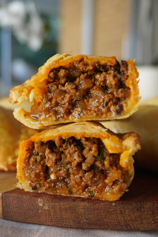 A photo showing two beef empanadas with golden, flaky pastry and a visible juicy beef filling with bits of olives and raisins.